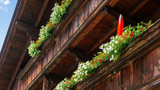 A wooden building with balconies adorned with flowers and red flags. - Cosy apartment for families (Alpbach)