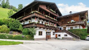 A traditional Alpine-style building with multiple balconies adorned with flowers, a stone foundation, and a staircase leading to the entrance. - Cosy apartment for families (Alpbach)
