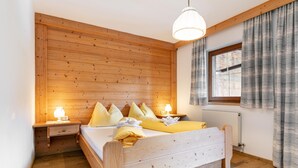 A wooden-paneled bedroom with a bed, bedside lamps, and a window with curtains. - Cosy apartment for families (Alpbach)