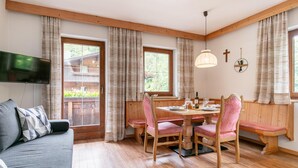A cozy dining area with wooden furniture, a television mounted on the wall, and large windows with curtains. - Beautiful apartments by the ski lift in Alpbach (Alpbach)