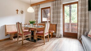 A dining area with wooden furniture, a table set for four, and a large window with curtains. - Beautiful apartments by the ski lift in Alpbach (Alpbach)