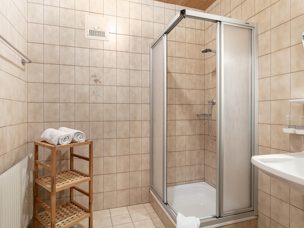A modern bathroom with a glass-enclosed shower, a wooden shelf with towels, and a white sink.