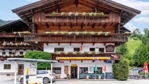 A traditional wooden building with balconies adorned with flowers, a Shell gas station in front, and a sign indicating a shop.