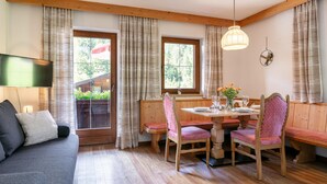 A cozy room with a wooden floor, a sofa, a dining table with chairs, and large windows with curtains.