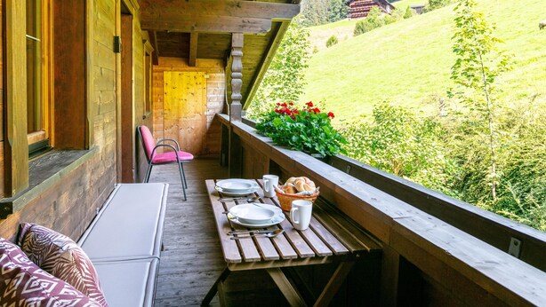 A wooden balcony with a table set for dining, overlooking a green valley and a mountain. - Right by the ski lift - 2 apartments in Alpbach (Alpbach)