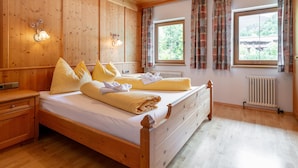 Quarto de madeira com cama, mesa de cabeceira, janela com cortinas e radiador.