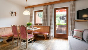 Uma sala de estar aconchegante com um banco de madeira, uma mesa de jantar com cadeiras, uma televisão e uma janela grande com cortinas.