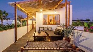 A covered outdoor seating area with a wooden bench, a sofa, and a table, surrounded by white walls and a wooden pergola. - New Stylish 4BR \ Rooftop Lounge \ 12min To Beach (Badung)
