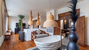 A modern bathroom with a large freestanding bathtub, wooden flooring, and a large mirror. - New Stylish 4BR \ Rooftop Lounge \ 12min To Beach (Badung)