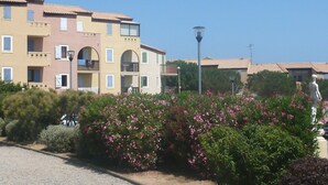 Un edificio con varios balcones, una estatua y un jardín lleno de flores rosadas.