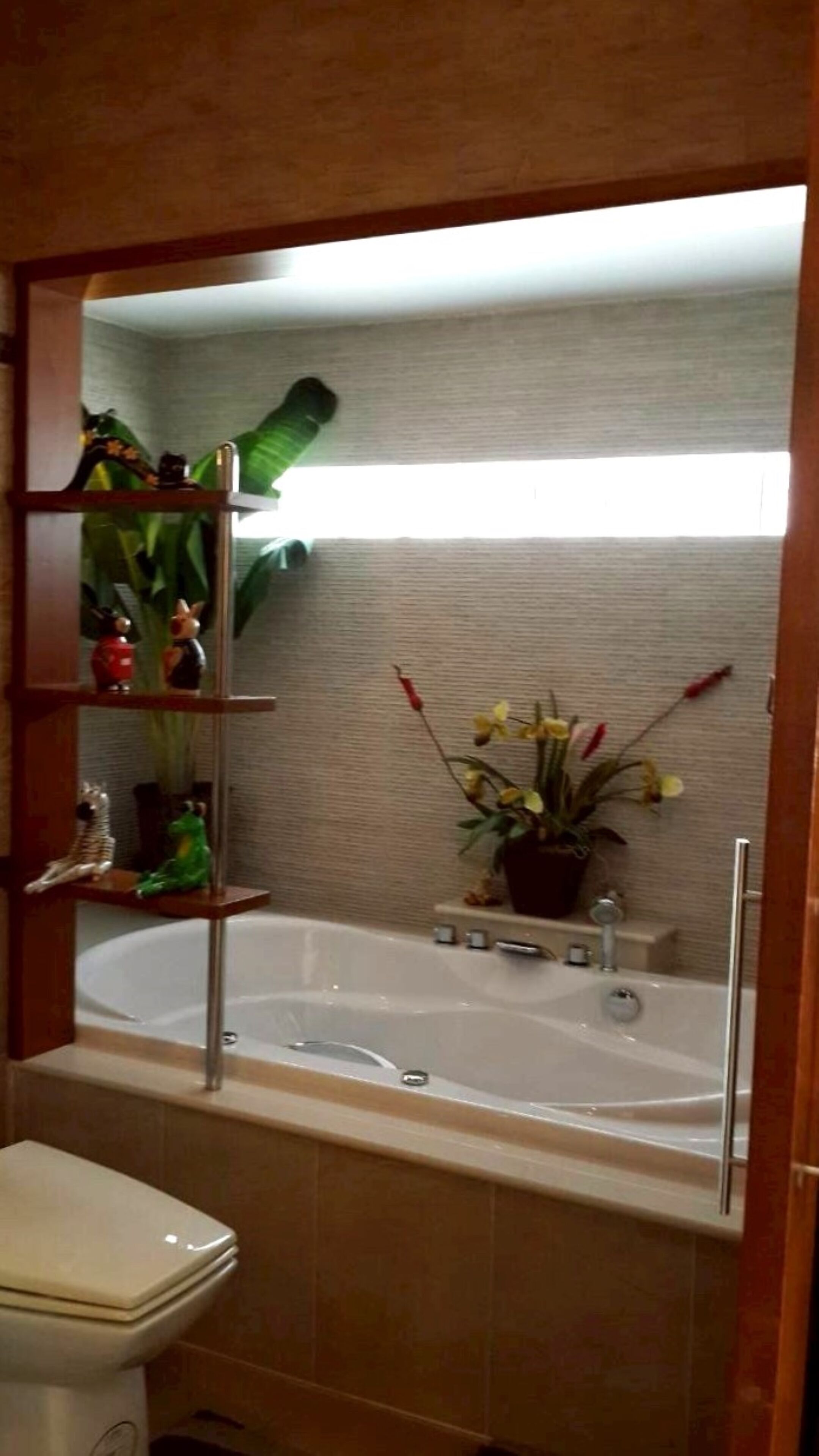 A bathroom with a bathtub, a toilet, and shelves with decorative items.