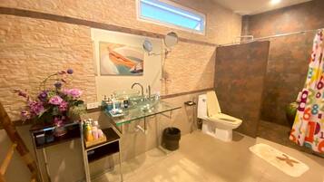 Un baño con lavamanos de vidrio, inodoro y zona de ducha.