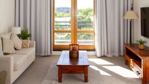En stue med sofa, sofabord, tv-møbel og et stort vindue med gardiner.