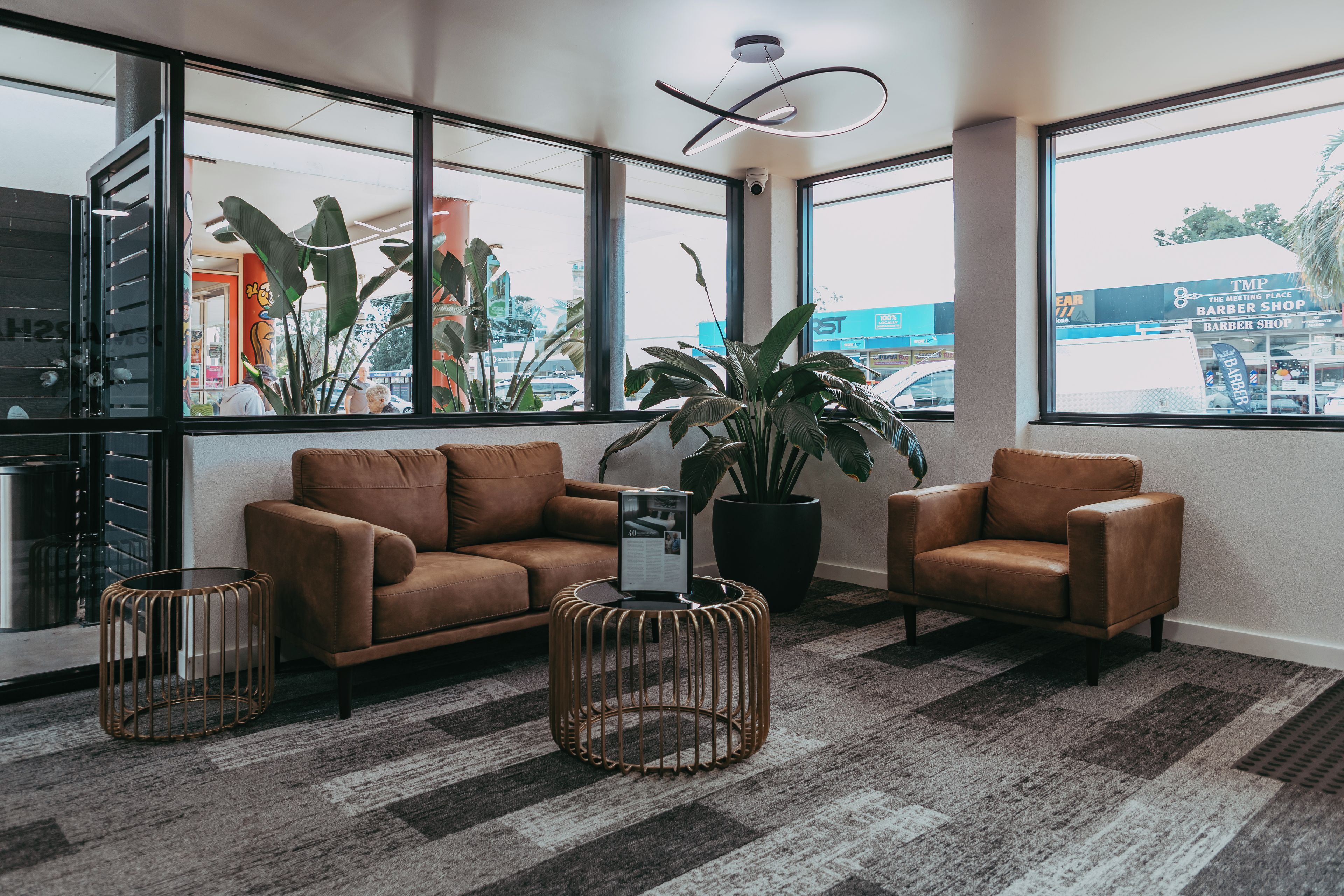 Een moderne lobby met leren banken, een grote potplant en een uitzicht op de stad door grote ramen.