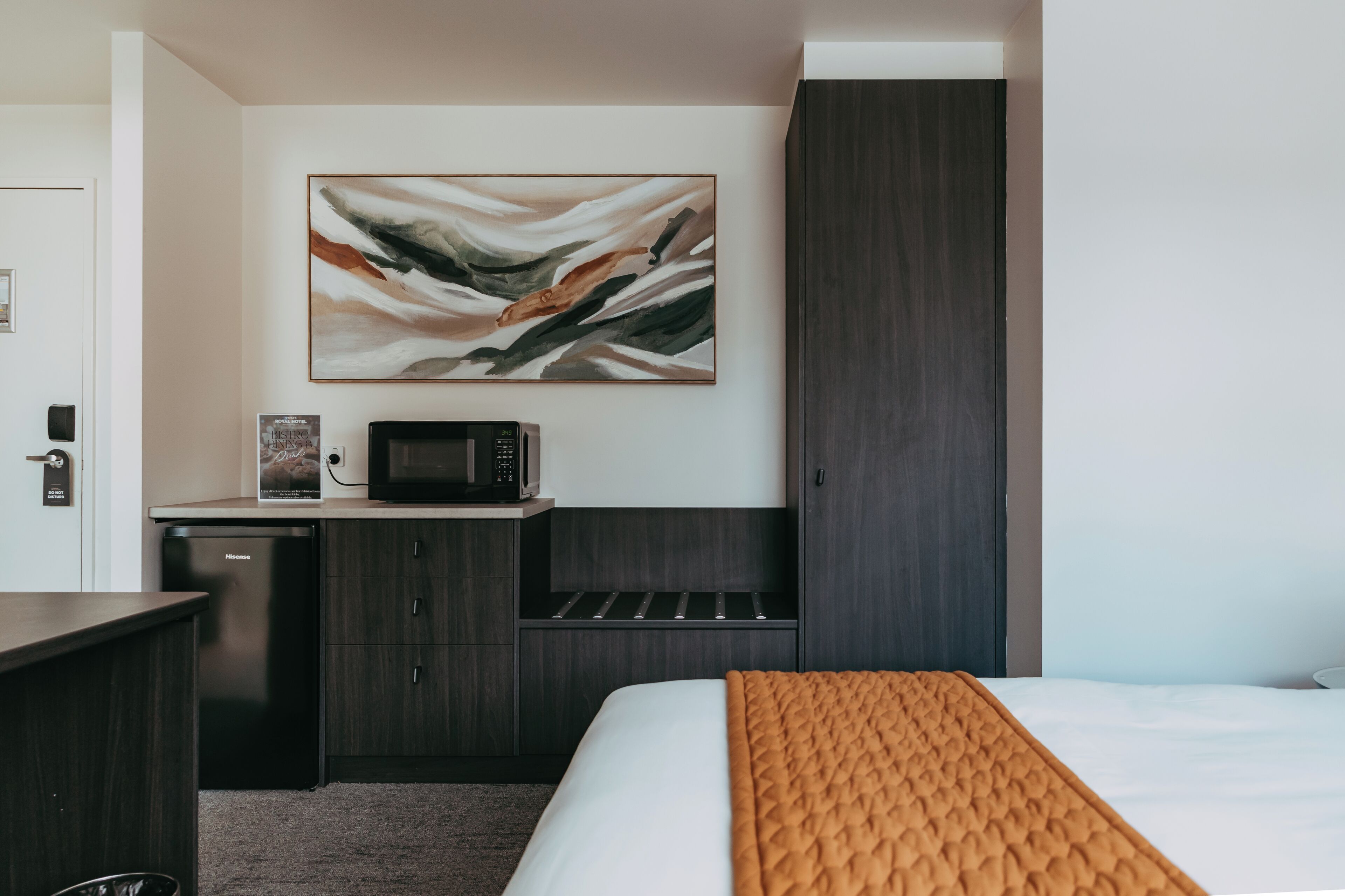 Una habitación de hotel con una cama, un microondas, una kitchenette pequeña y un cuadro en la pared.