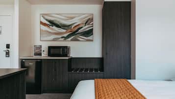 Una habitación de hotel con una cama, un microondas, una kitchenette pequeña y un cuadro en la pared.