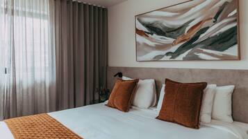Habitación de hotel con una cama grande, cabecera, un cuadro y una ventana con cortinas.