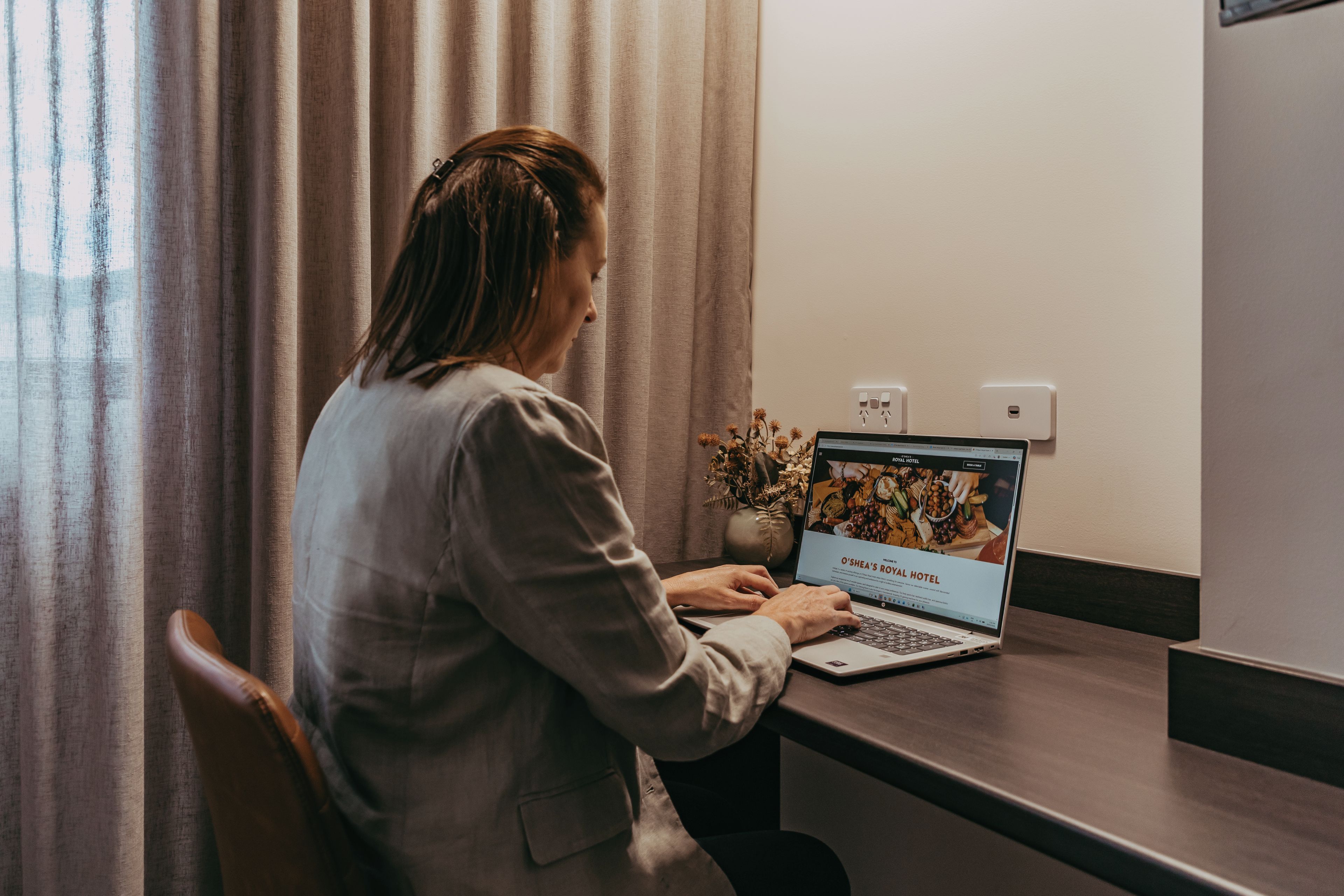 A person using a laptop at a desk with a laptop screen displaying a hotel website.