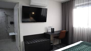 A hotel room with a bed, a desk, a chair, a TV, a shower, and a window with curtains.