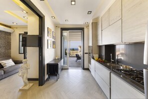 A modern kitchen with a view to the outside, a dining area with a statue, and a living room with a sofa and artwork. - 3BR Sorrento Apt with SeaView Terrace (Sorrento)