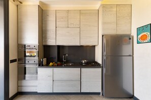 A modern kitchen with light wood cabinets, stainless steel appliances, and a built-in oven.