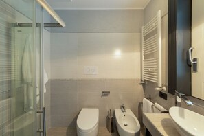 A modern bathroom with a glass shower enclosure, a toilet, a bidet, and a sink with a mirror.