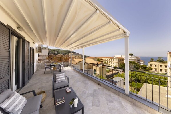 A balcony with a view of the sea, furnished with a sofa, chairs, and a table.