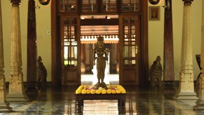 A statue on a platform with flowers, surrounded by columns in a hallway. - Svatma Mayavaram (Kuthalam)