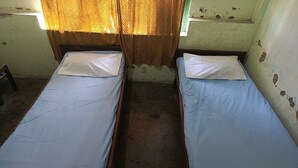 Two single beds with wooden frames and blue bedding in a room with peeling paint on the walls and a window with a patterned curtain. - Hotel O Agung Banjarnegara (Banjarnegara)