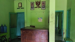 A reception desk in a room with green walls, a clock, and two framed portraits above it. - Hotel O Agung Banjarnegara (Banjarnegara)
