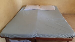 A single bed with a blue mattress and white pillows in a room with plain yellow walls. - Hotel O Agung Banjarnegara (Banjarnegara)