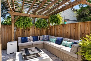 Un espace extérieur abrité, doté d’une pergola en bois, de bancs rembourrés et d’une petite table.
