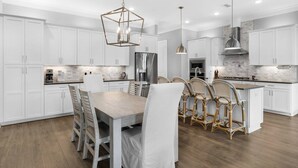 Una cocina moderna con armarios blancos, una isla central y un área de comedor con sillas de mimbre.