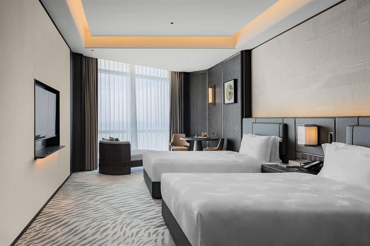 A hotel room with two beds, a desk, a chair, and a small table.