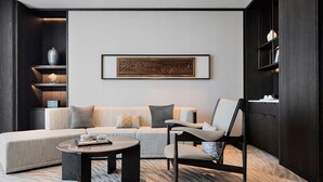 A modern living room with a sectional sofa, a round coffee table, and a minimalist chair. There is a framed artwork on the wall and shelves with decorative items. - WHITE SWAN HOTEL SHANTOU (Shantou)