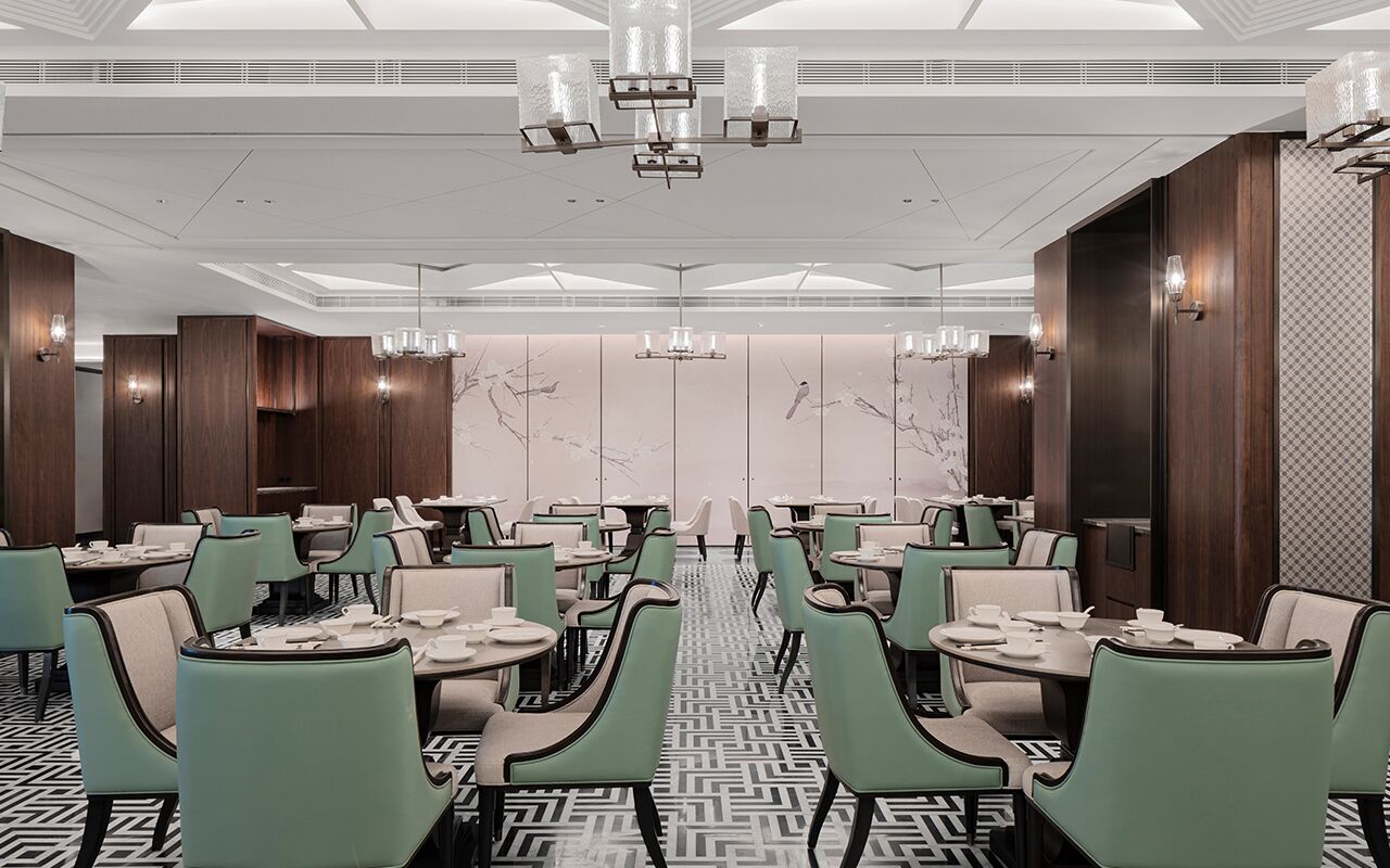 A modern restaurant with green chairs, marble backdrops, and pendant lighting.