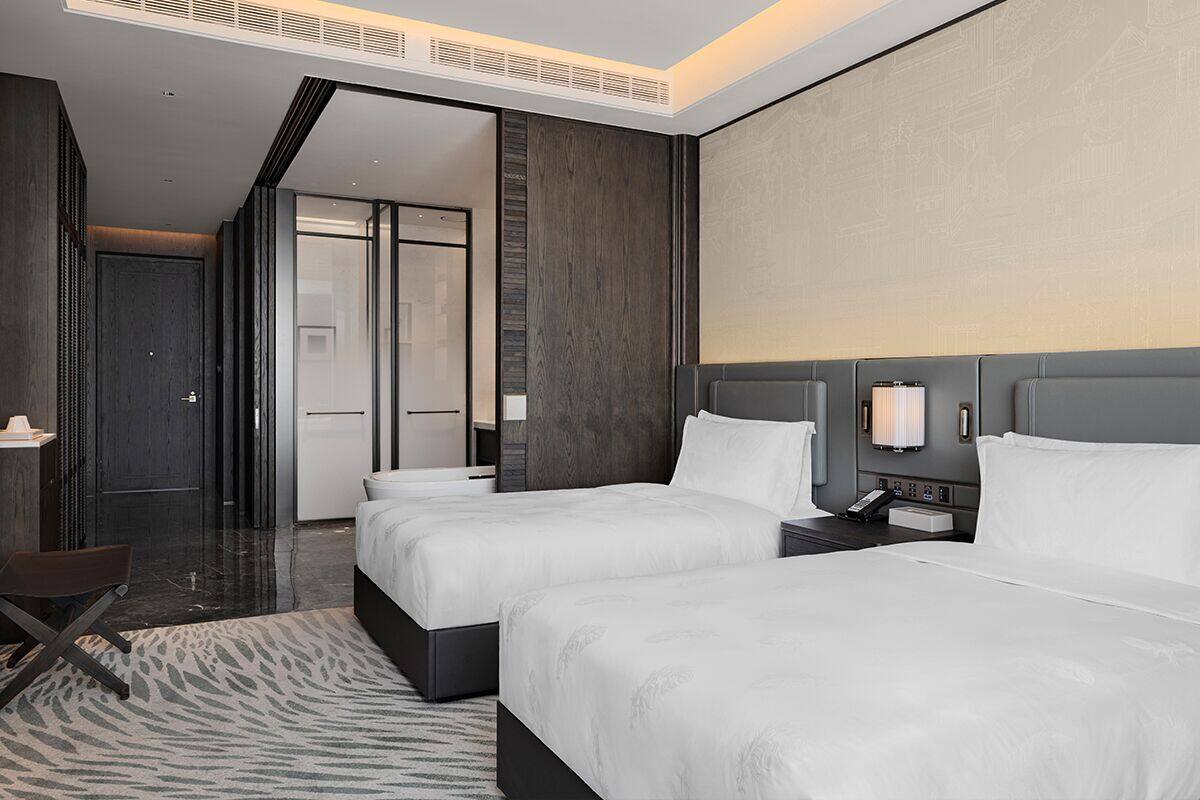 A hotel room with two beds, a desk, and a chair.