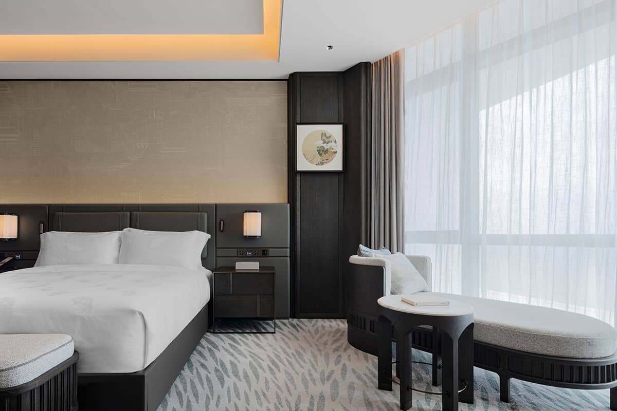 A modern hotel room with a large bed, bedside tables, a desk, and a chair.
