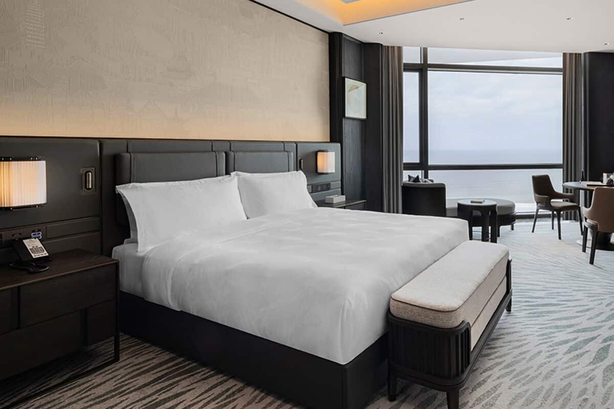 A hotel room with a large bed, bedside tables, a desk, and a view of the sea.