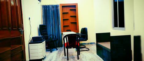 A compact office space with a desk, two chairs, a filing cabinet, a shelf unit, and a window.