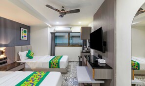 A hotel room with two beds, a TV, a desk, and a ceiling fan.