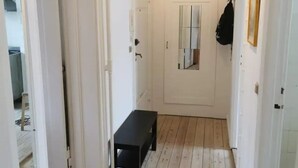 Un pasillo estrecho con suelo de madera, un banco y una puerta con espejo.
