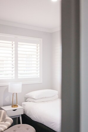 A bedroom with a bed, a bedside table with a lamp, and a window with blinds. - 42 Banksia by the BnB Collection (Centennial Park)