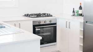 A modern kitchen with white cabinetry, a gas stove, an oven, and a refrigerator. - 42 Banksia by the BnB Collection (Centennial Park)