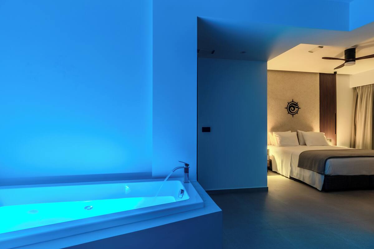 A modern hotel room with a large bathtub, a bed with a headboard, and a ceiling fan.
