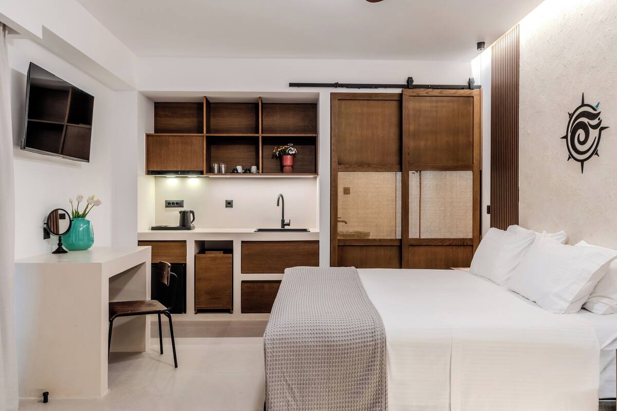 A compact hotel room with a kitchenette, a bed, a desk, and a chair.