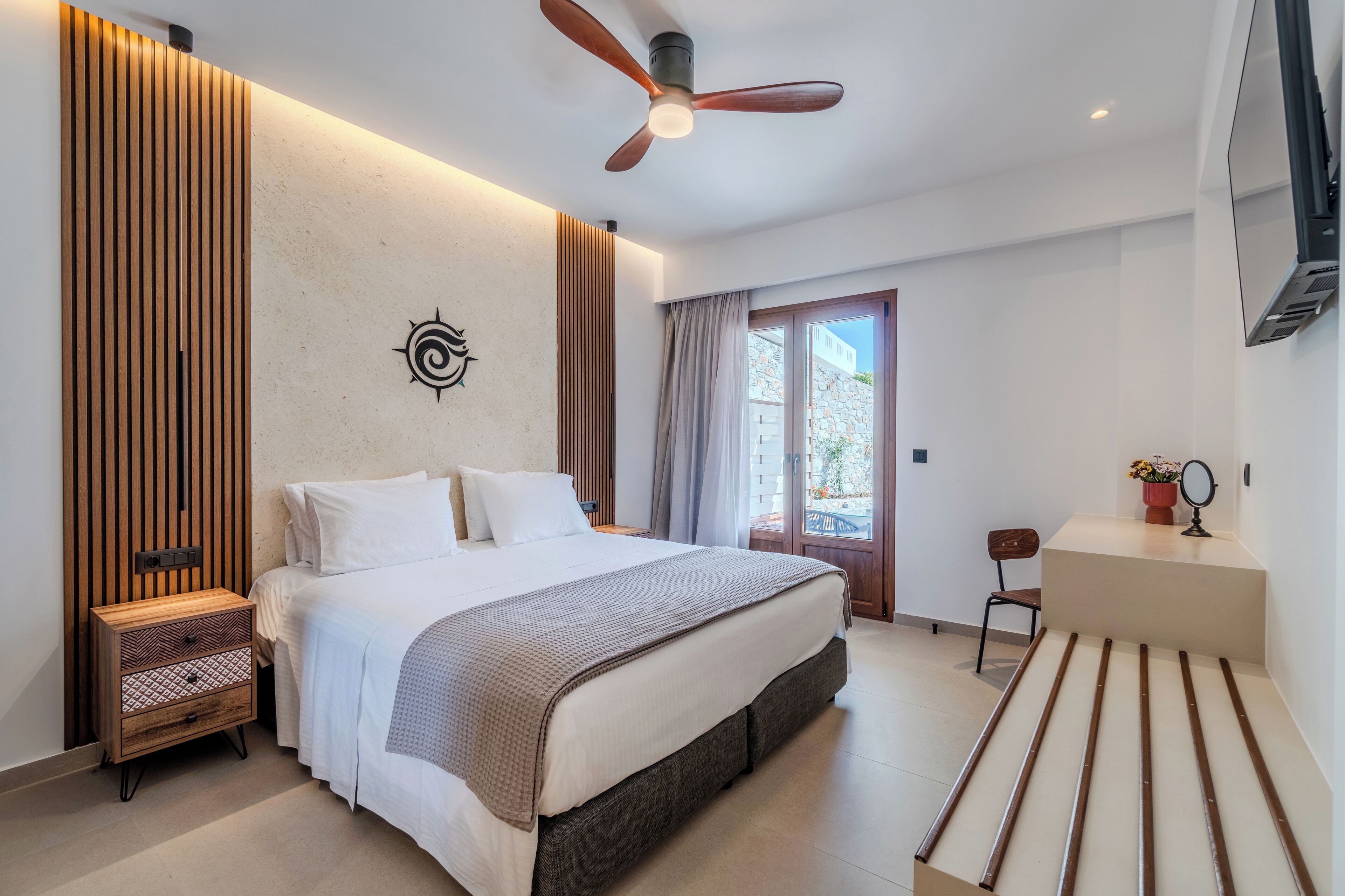 A modern bedroom with a bed, wooden panel wall, ceiling fan, and a view of the outdoors.