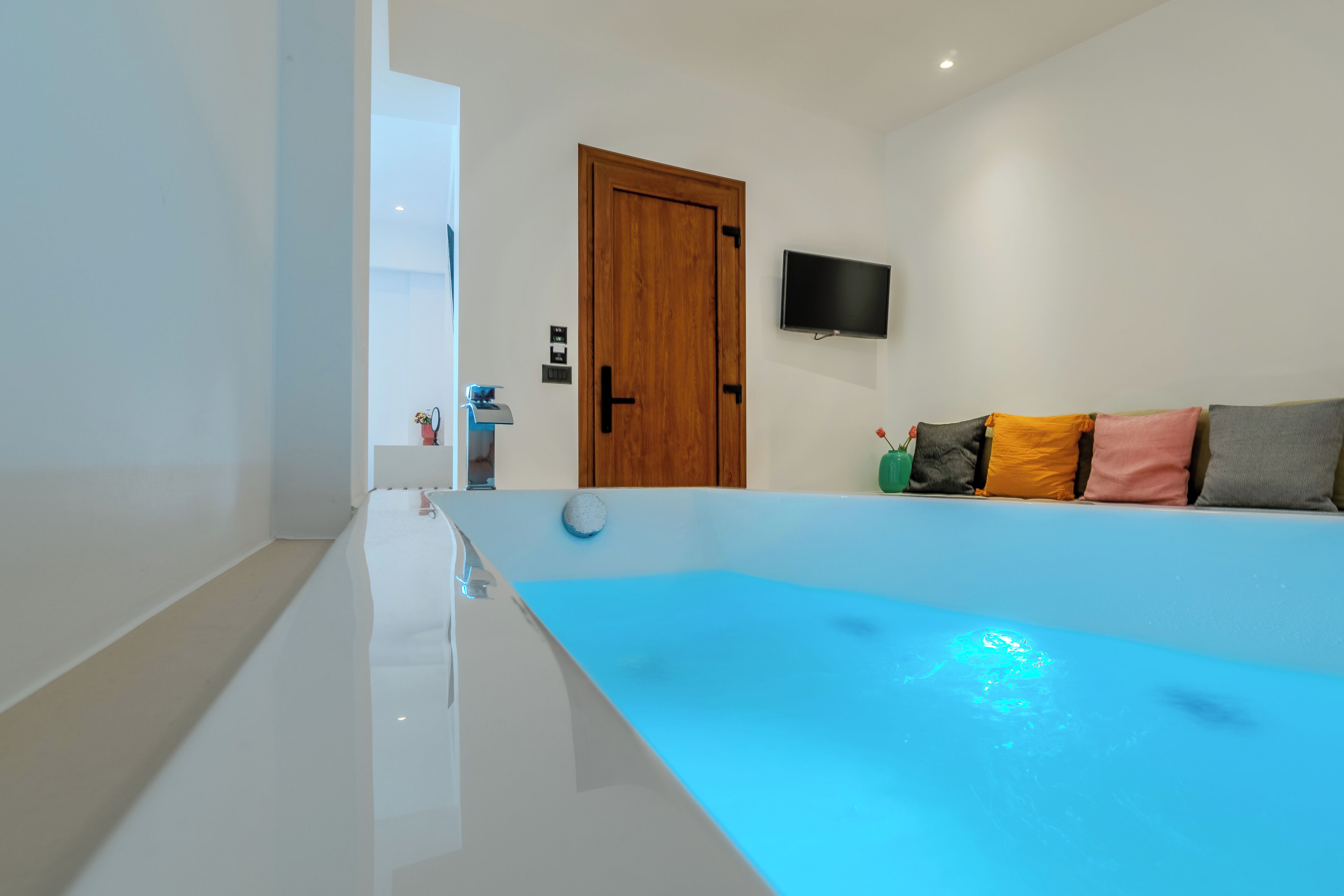 Un baño moderno con una bañera grande, una puerta de madera y un televisor de pantalla plana montado en la pared.