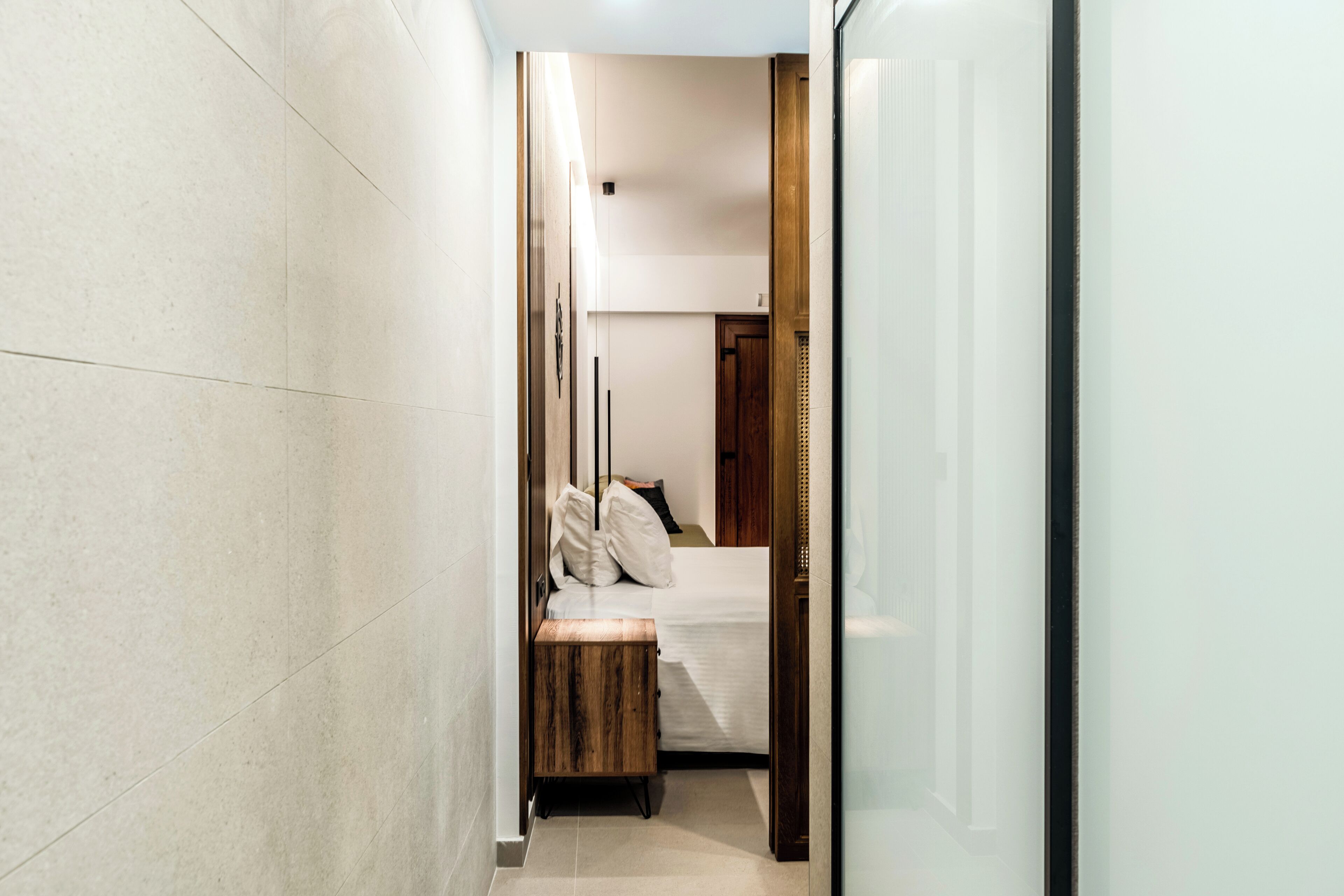 Un pasillo estrecho que conduce a un dormitorio con cama, mesita de noche y un banco de madera.