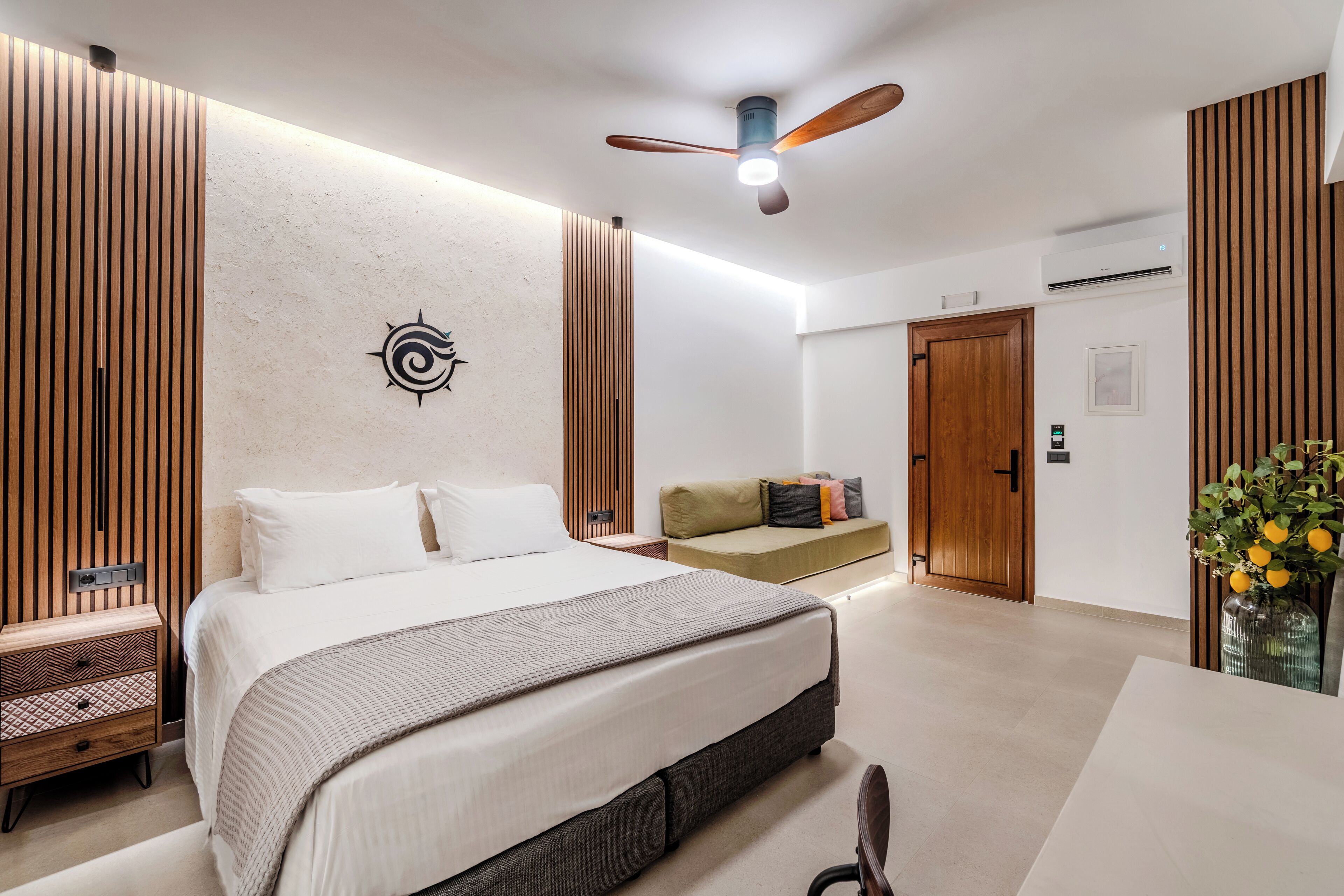 A modern bedroom with a large bed, a ceiling fan, a wooden wall panel, a bedside table, and a nightstand.